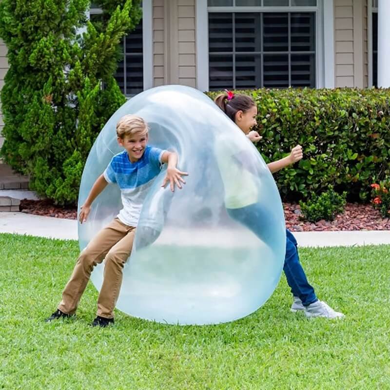Boy and a girl playing with a huge squishy and bouncy wobble ball outside their house.